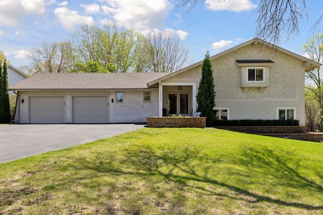 tri-level home featuring french doors, a garage, driveway, a front lawn, and stucco siding