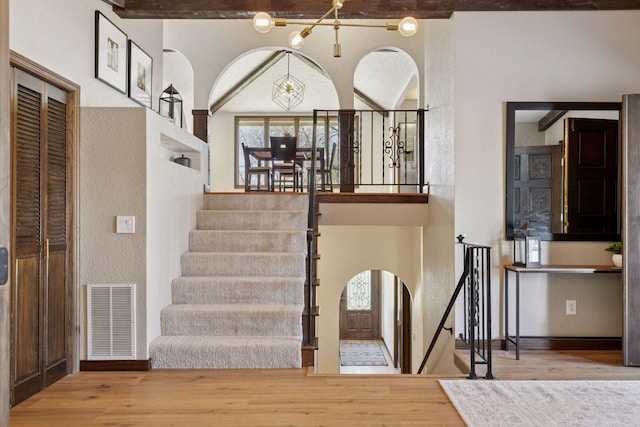 stairs with arched walkways, wood finished floors, and beamed ceiling