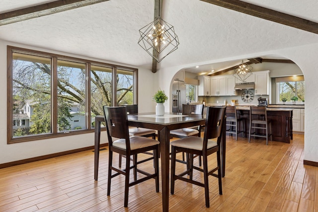 dining room featuring arched walkways, a textured ceiling, light wood-type flooring, and plenty of natural light