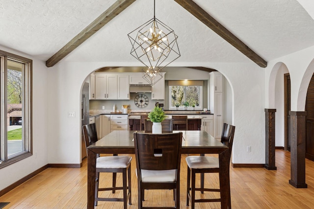 dining room with beamed ceiling, a textured ceiling, light wood-type flooring, a chandelier, and arched walkways