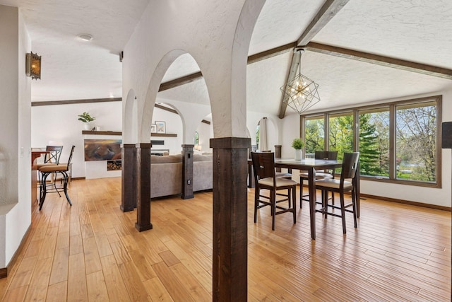 dining area with arched walkways, a textured ceiling, light wood-style floors, baseboards, and a chandelier
