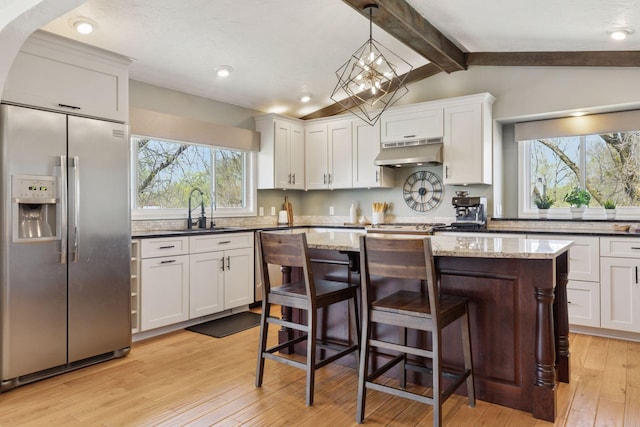 kitchen with stainless steel refrigerator with ice dispenser, under cabinet range hood, a sink, light wood-style flooring, and white cabinetry