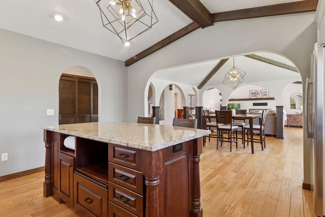 kitchen with arched walkways, light wood-type flooring, freestanding refrigerator, a chandelier, and light stone countertops