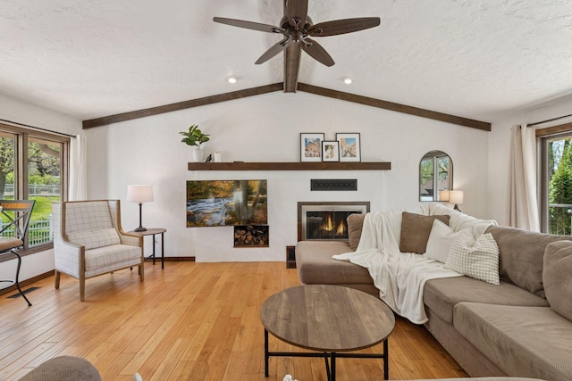 living room featuring a textured ceiling, light wood-style floors, ceiling fan, a glass covered fireplace, and baseboards