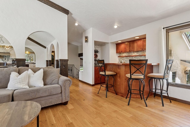 living room featuring arched walkways, light wood-type flooring, and baseboards