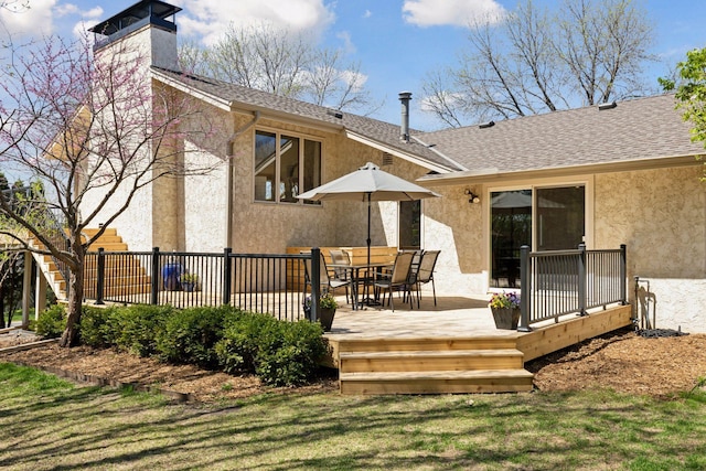 rear view of property with stucco siding, a shingled roof, a chimney, and a wooden deck