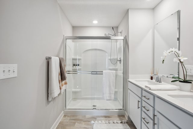 bathroom featuring a shower stall, double vanity, baseboards, and recessed lighting