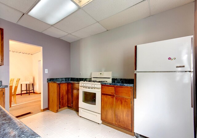 624 Main St, West Concord, MN 55985 - kitchen featuring white appliances, a drop ceiling, brown cabinets, light floors, and dark stone countertops