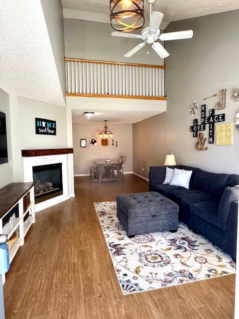 living area featuring high vaulted ceiling, ceiling fan, wood finished floors, a glass covered fireplace, and baseboards
