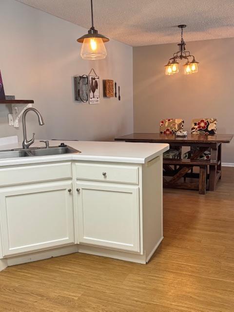 kitchen featuring a sink, a peninsula, light wood-style flooring, and a textured ceiling