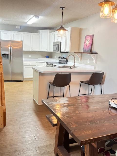 kitchen featuring stainless steel appliances, a peninsula, light wood finished floors, a sink, and a textured ceiling