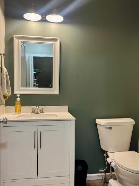 half bathroom featuring toilet, vanity, and baseboards