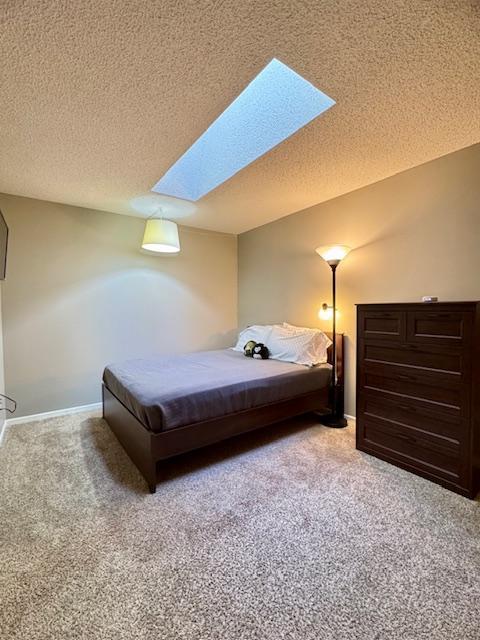 bedroom with a skylight, light carpet, a textured ceiling, and baseboards