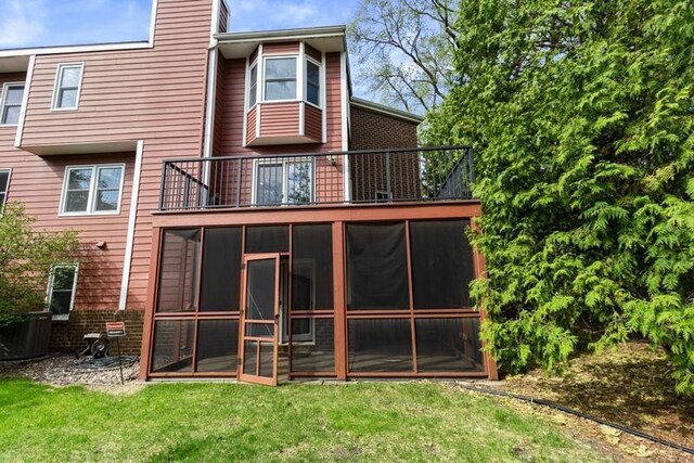 rear view of property with a balcony, a yard, central AC unit, and a sunroom