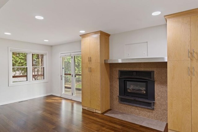 unfurnished living room with wood finished floors, a tiled fireplace, baseboards, and recessed lighting