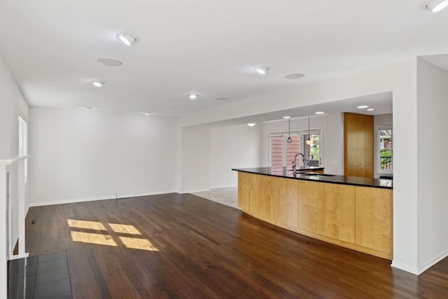 unfurnished living room with dark wood-type flooring, a sink, baseboards, and recessed lighting