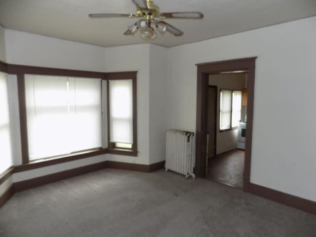 carpeted empty room with radiator, baseboards, and a ceiling fan