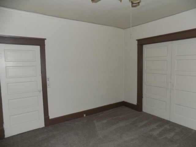 unfurnished bedroom with dark carpet, a closet, and baseboards