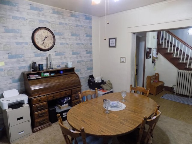 dining space featuring radiator heating unit, stairway, ceiling fan, and wood walls