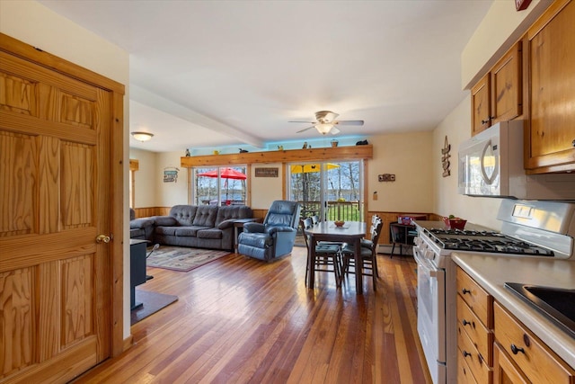 25185 Moreau Rd, Aitkin, MN 56431 - kitchen with white appliances, dark wood-style flooring, ceiling fan, brown cabinetry, and a wainscoted wall