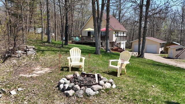 25185 Moreau Rd, Aitkin, MN 56431 - view of grassy yard featuring an outdoor fire pit, an outdoor structure, a detached garage, and a deck