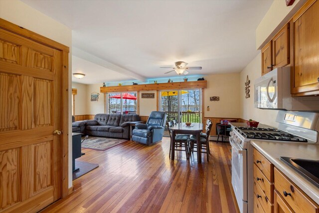25185 Moreau Rd, Aitkin, MN 56431 - kitchen with gas range, white microwave, dark wood-type flooring, a ceiling fan, and brown cabinets