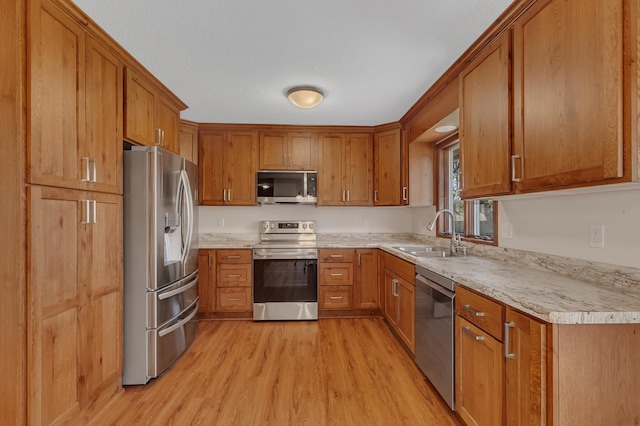 kitchen featuring stainless steel appliances, a sink, light wood-style flooring, and brown cabinets