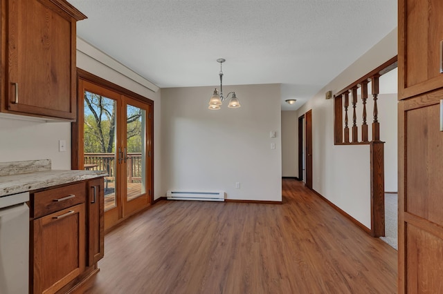 unfurnished dining area with baseboard heating, wood finished floors, a chandelier, a textured ceiling, and baseboards