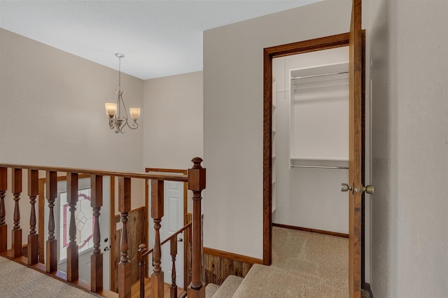 hallway featuring carpet flooring, an upstairs landing, baseboards, and a chandelier