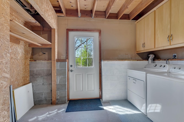 clothes washing area featuring independent washer and dryer, cabinet space, and a wainscoted wall