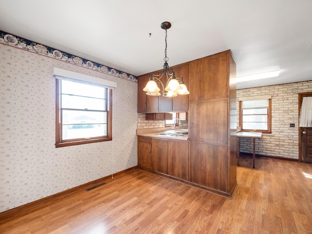 116 California Ave, Morris, MN 56267 - kitchen with a chandelier, brown cabinetry, light wood-type flooring, plenty of natural light, and wallpapered walls