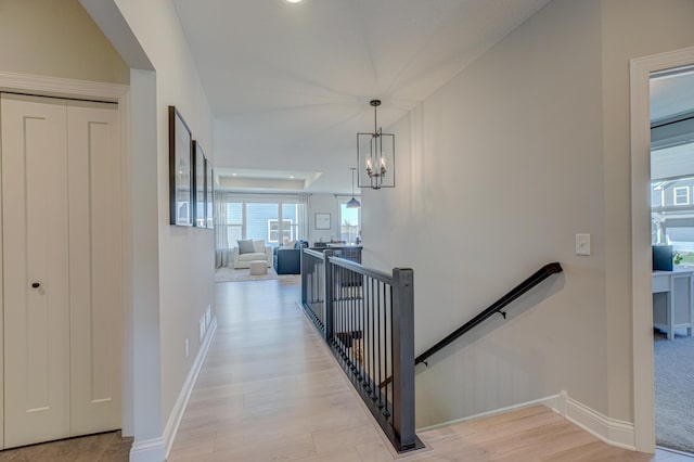 hallway with an upstairs landing, a chandelier, light wood finished floors, and baseboards
