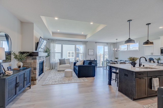 living area featuring light wood-style floors, a fireplace, a tray ceiling, a chandelier, and recessed lighting