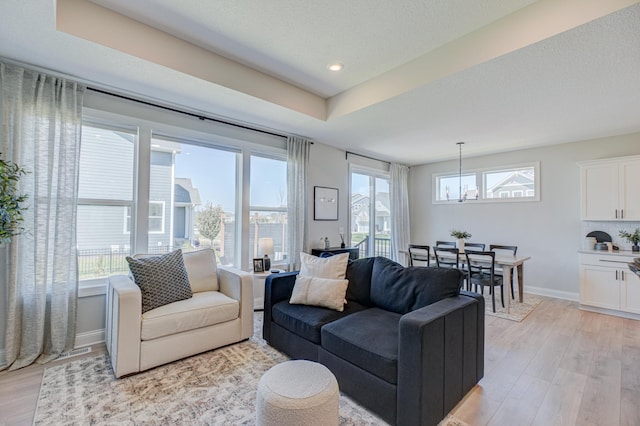 living room featuring light wood-type flooring, a chandelier, baseboards, recessed lighting, and a tray ceiling