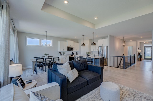 living area with a chandelier, light wood finished floors, baseboards, recessed lighting, and a raised ceiling