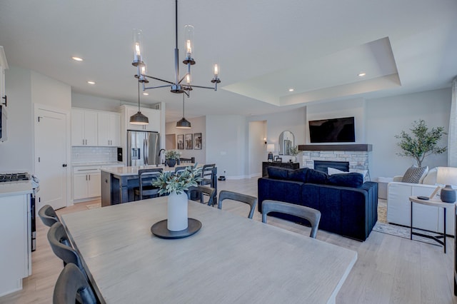 dining space featuring a tray ceiling, light wood-style flooring, a fireplace, recessed lighting, and a chandelier
