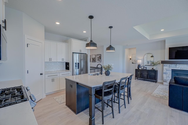 kitchen with stainless steel fridge with ice dispenser, a sink, open floor plan, light wood finished floors, and white cabinetry