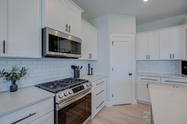 kitchen featuring appliances with stainless steel finishes, white cabinets, light wood-type flooring, decorative backsplash, and recessed lighting