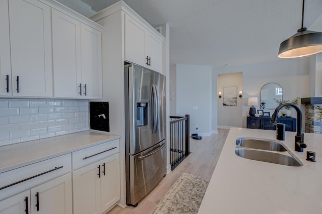 kitchen featuring stainless steel refrigerator with ice dispenser, backsplash, a sink, a textured ceiling, and light countertops