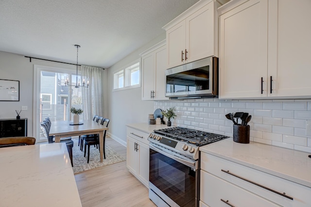 kitchen featuring stainless steel appliances, a chandelier, light wood-type flooring, backsplash, and white cabinetry
