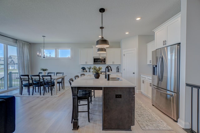 kitchen with appliances with stainless steel finishes, a sink, a chandelier, light countertops, and light wood-type flooring