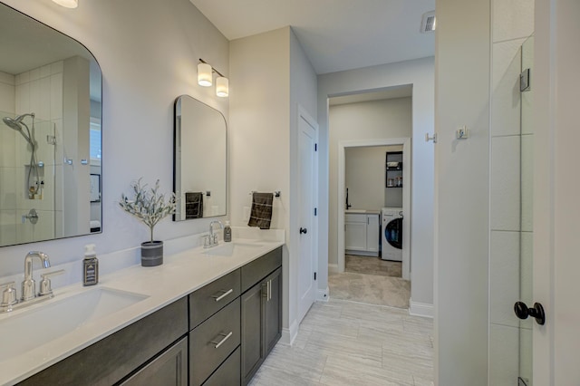 full bathroom featuring a tile shower, washer / dryer, double vanity, and baseboards
