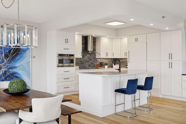 kitchen with stainless steel oven, wall chimney range hood, light wood-type flooring, tasteful backsplash, and recessed lighting