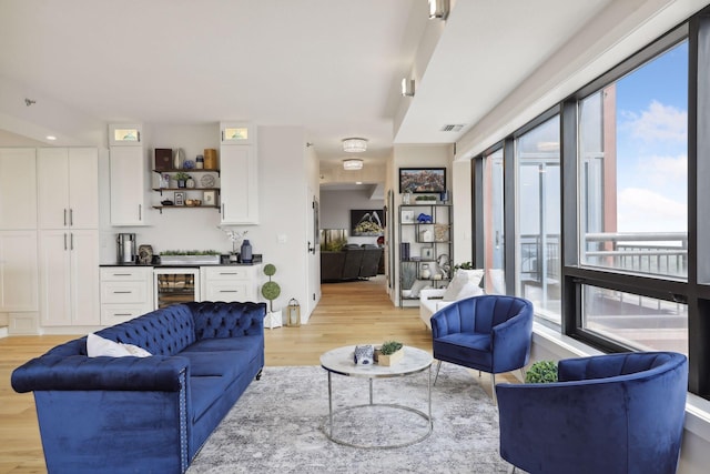 living area featuring light wood-style flooring, beverage cooler, and bar