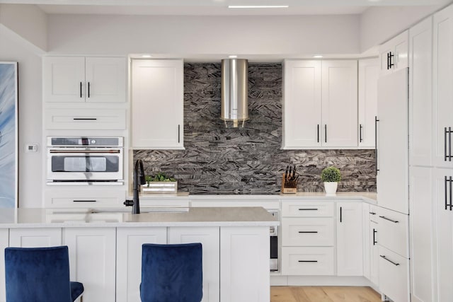 kitchen featuring oven, wall chimney range hood, gas cooktop, and white cabinets