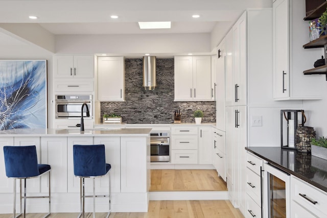 kitchen with oven, wall chimney range hood, beverage cooler, open shelves, and recessed lighting