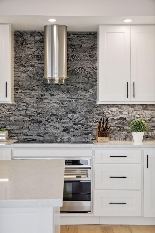 kitchen with stainless steel oven, decorative backsplash, light countertops, white cabinets, and black electric stovetop