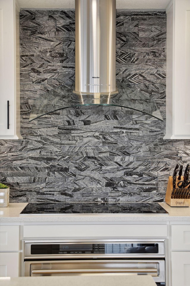 kitchen view of decorative backsplash, white cabinetry, and light countertops