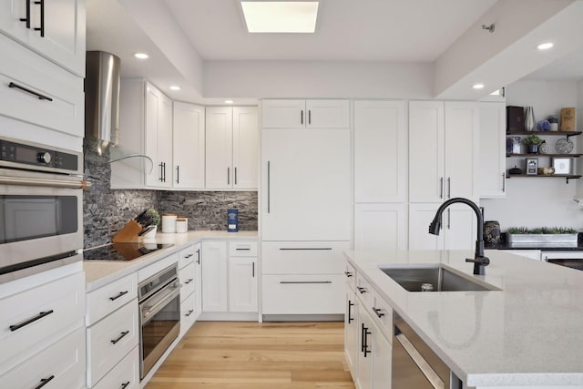 kitchen with appliances with stainless steel finishes, a sink, recessed lighting, light wood-type flooring, and white cabinetry