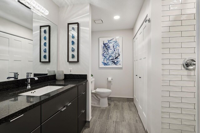 bathroom featuring baseboards, wood finished floors, toilet, vanity, and recessed lighting